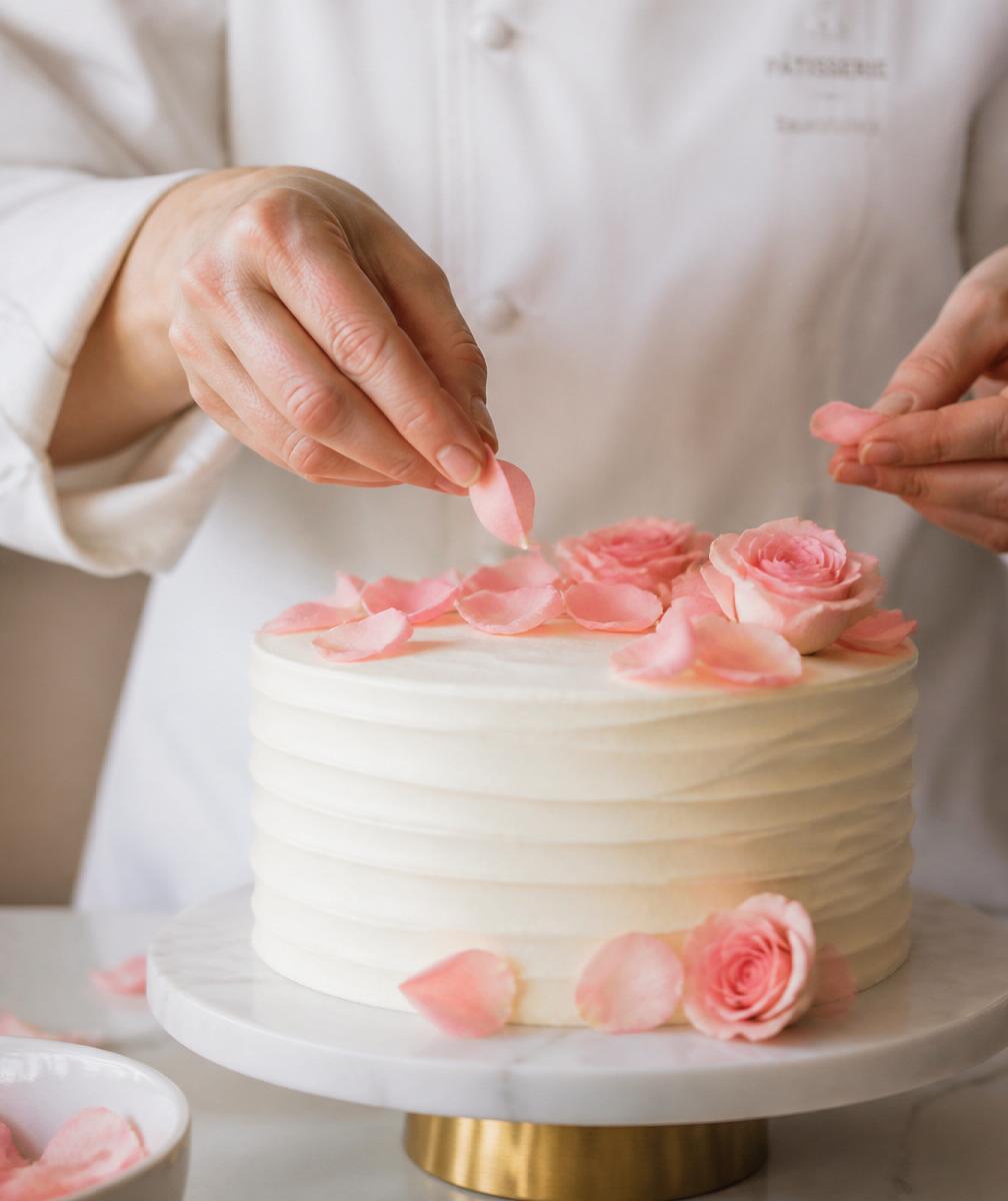 Chef decorando a mano un pastel con pétalos de rosa